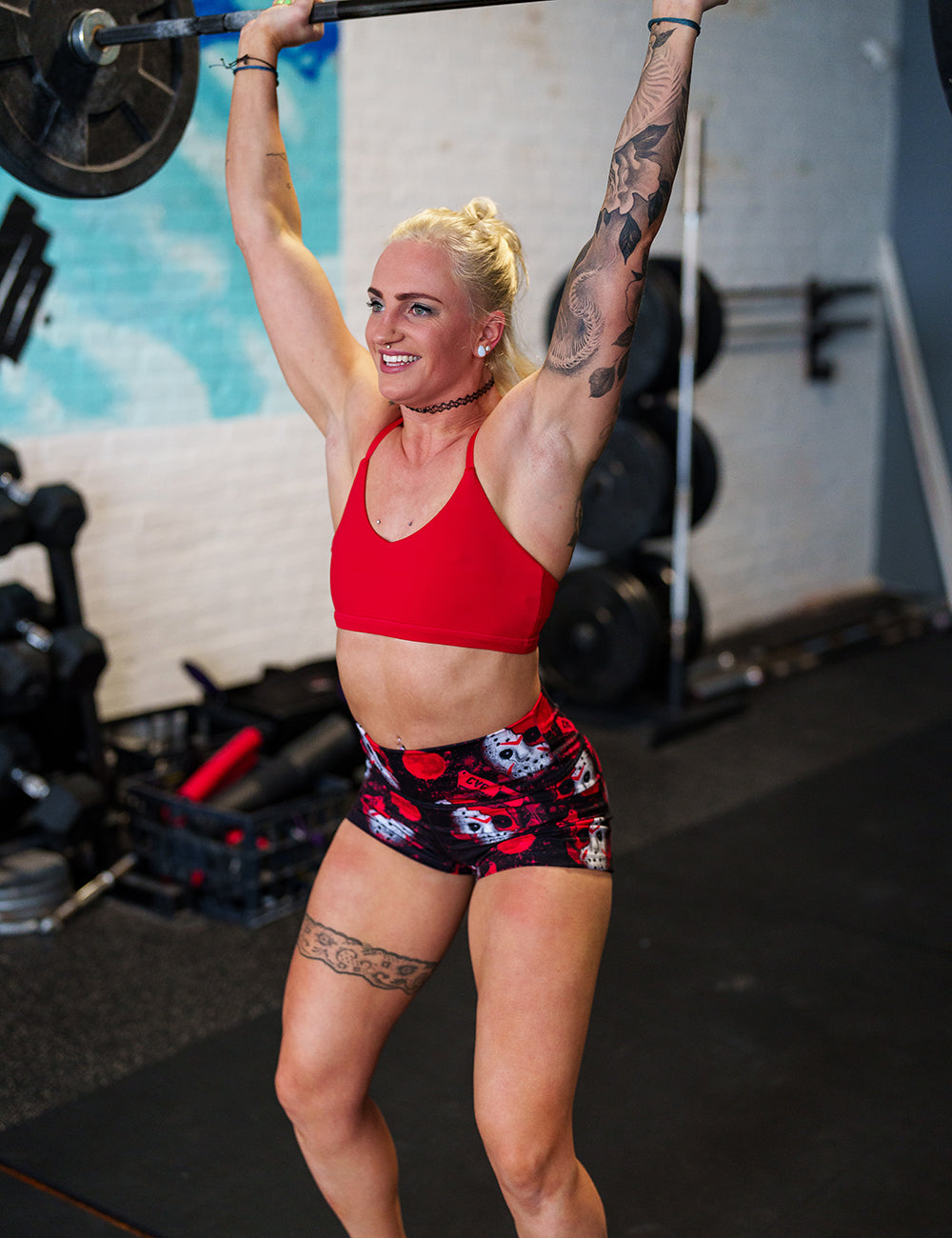 model wearing the bloody hocky mask 2.5 inch shorts and red sports bra lifting weights in the gym