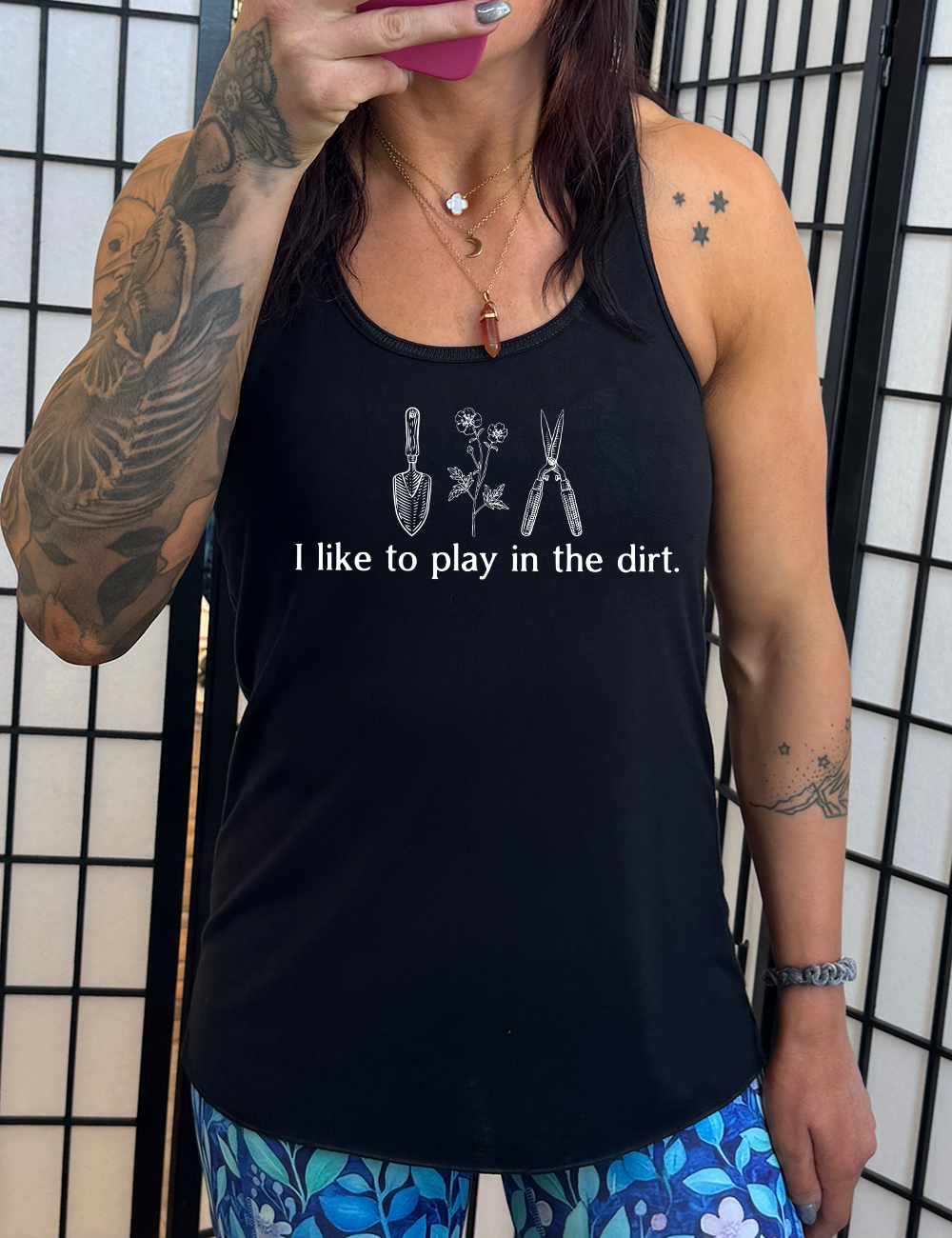 black flowy racerback tank with the words "I like to play in the dirt." on it with the graphic of a hand trowel, two flowers, and shears
