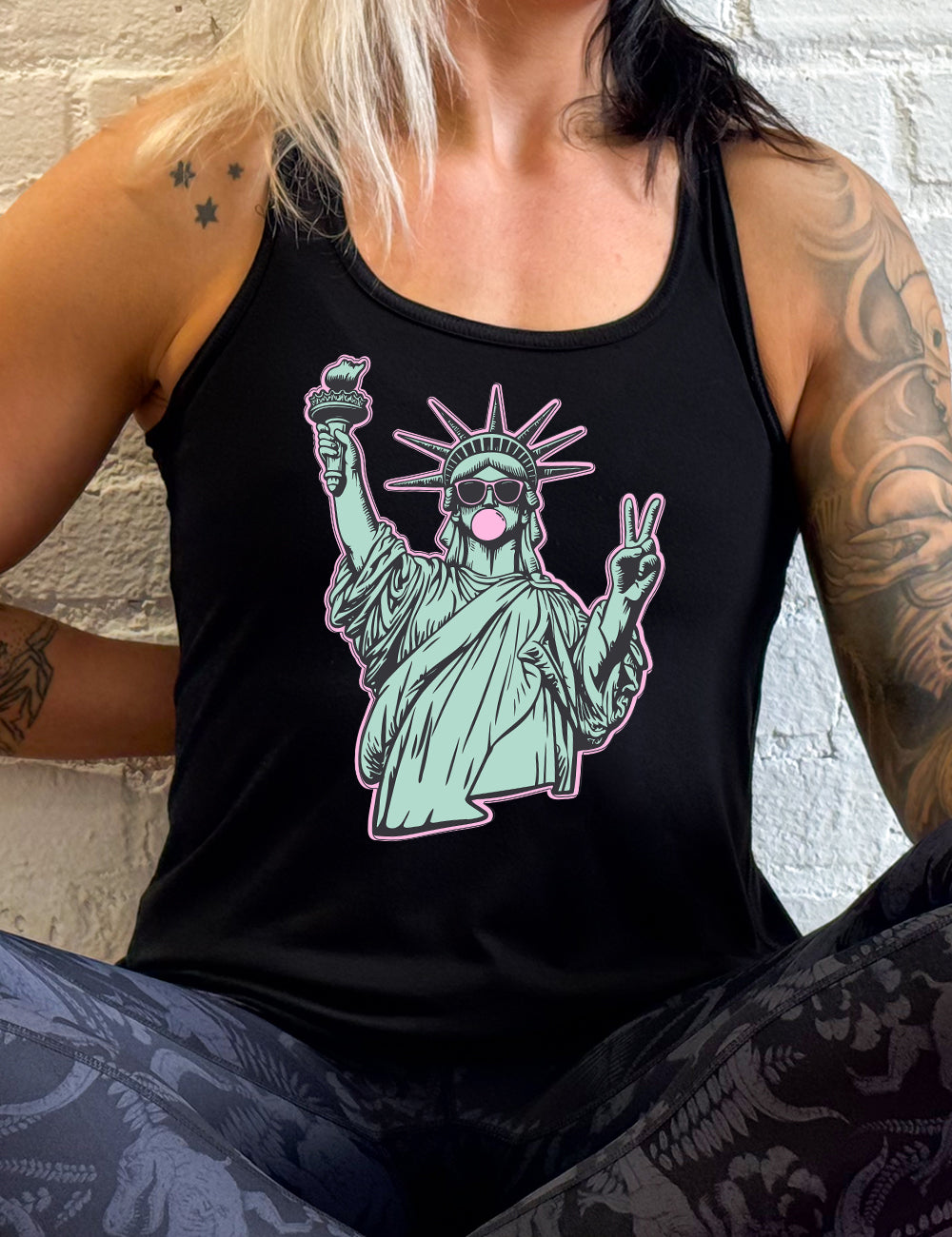 black flowy racerback tank with the graphic of the statue of liberty, wearing sunglasses, blowing a gum bubble, and giving the peace sign