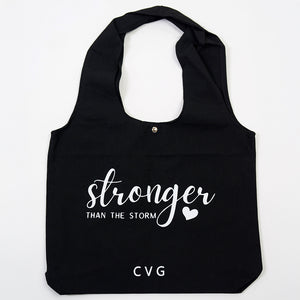 "stronger than the storm" saying on a black tote bag