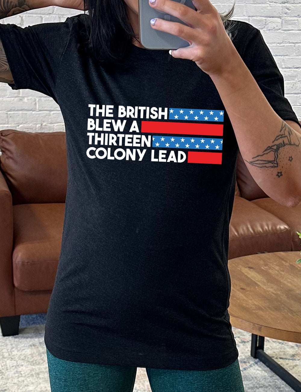 black unisex tee with the words "the British" (and a blue starred bar finishing the space to the right), then below "blew a" (and a red bar), then below "thirteen" (and a blue starred bar),  and below "colony lead" (and a red bar)