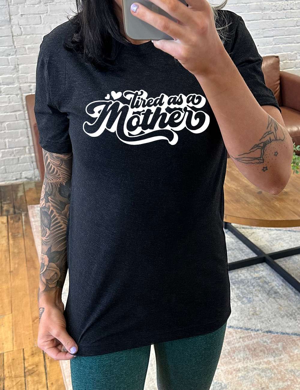 black unisex tee with the words "tired as a mother' on it, with a couple little hearts at the start