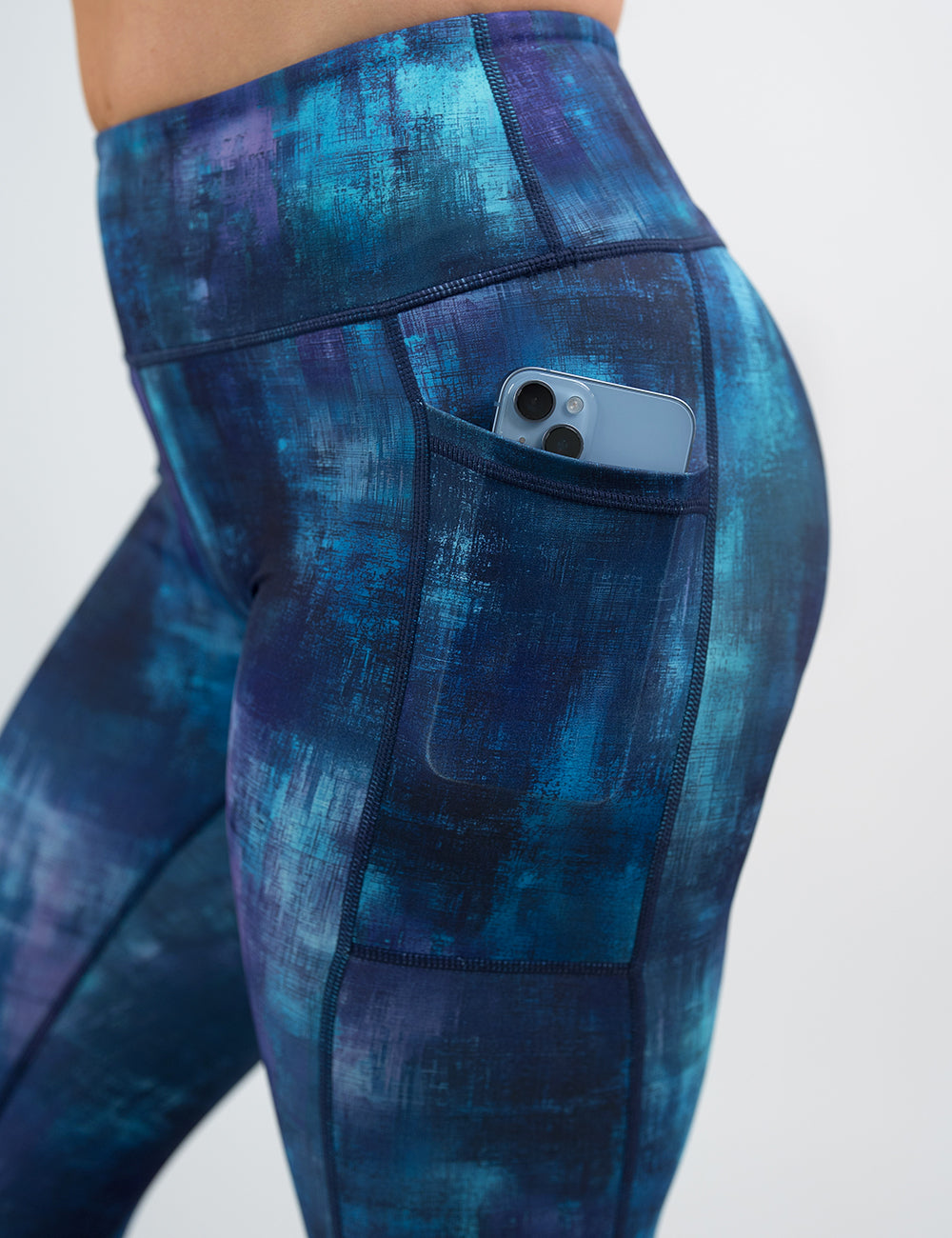 close up of the blue, teal, and purple grunge concrete pattern leggings with a phone in its pocket