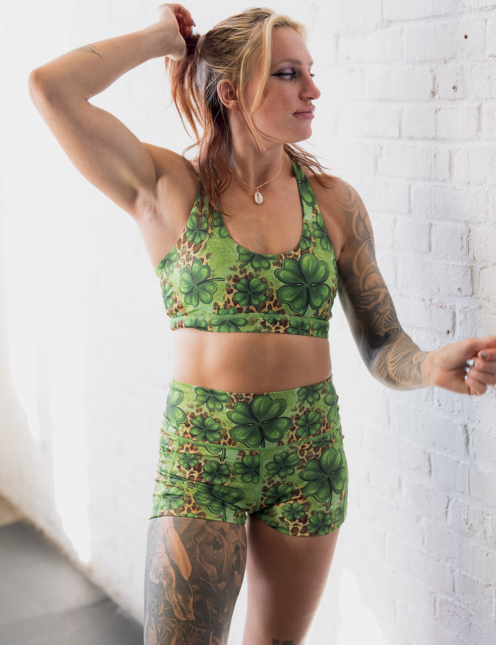 model wearing the 2.5 inch clover pattern against a cheetah print and green background shorts and bra against a white brick backdrop