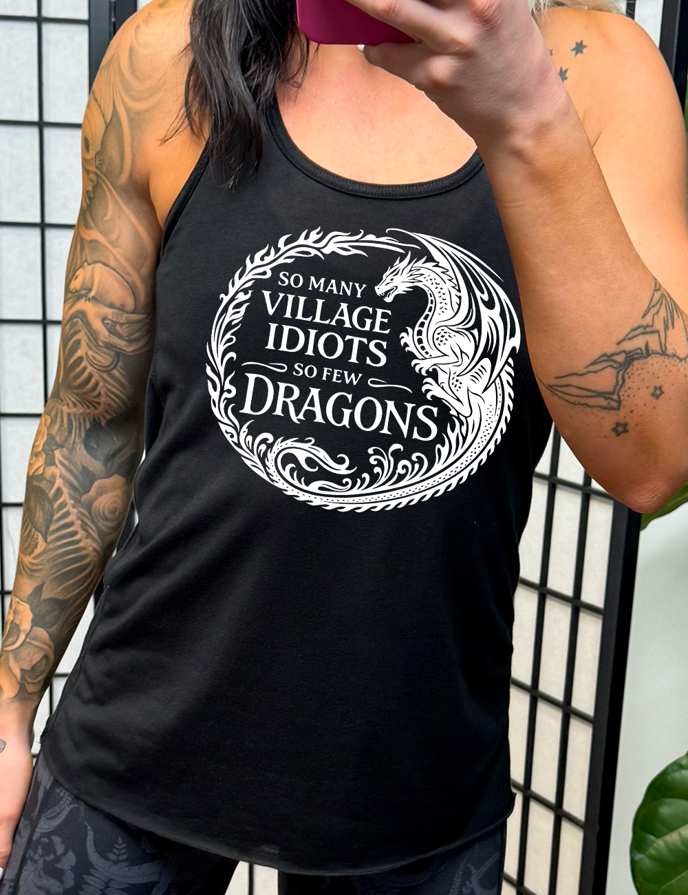 black racerback tank with the graphic of a dragon, creating a circle from its tail plus flames, and the words "so many village idiots so few dragons" written within it