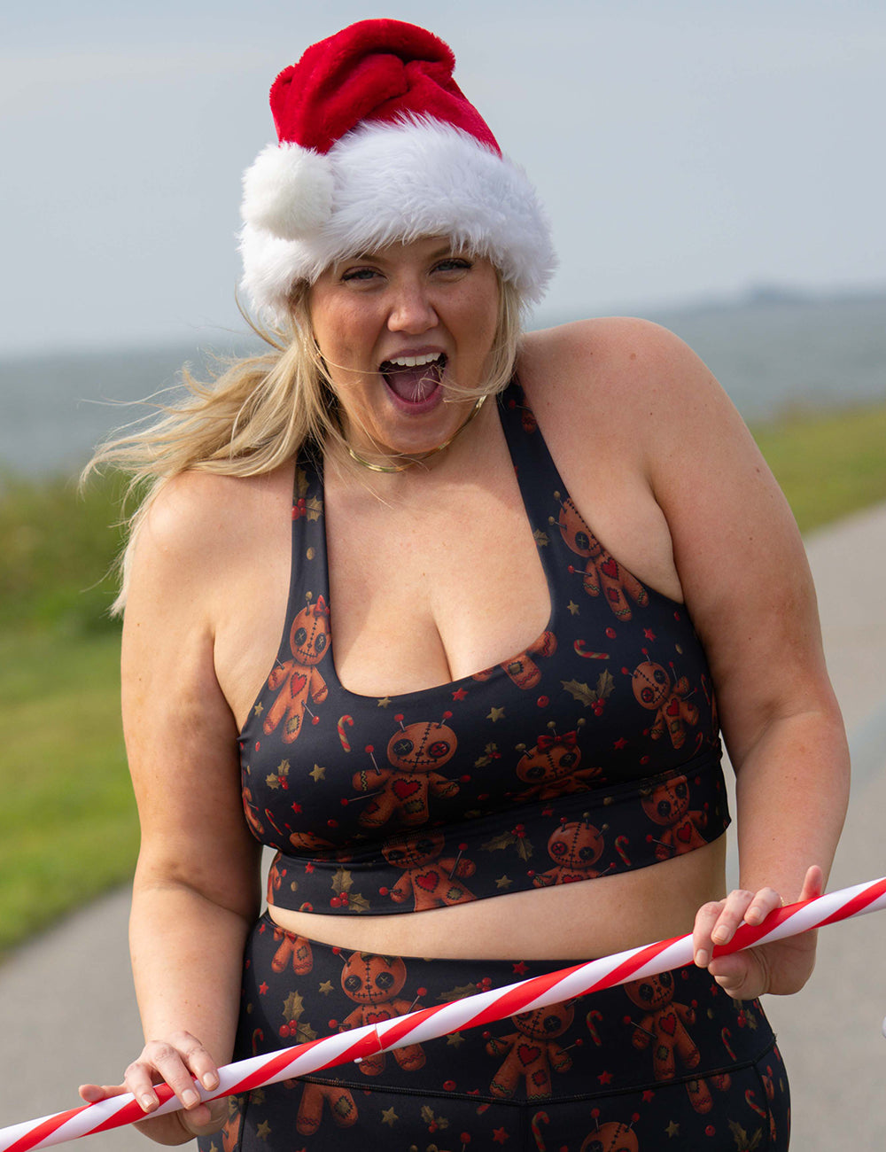 model wearing the gingerbread voodoo dolls with pins in them surrounded by berries and stars on a black background sports bra holding a candy cane