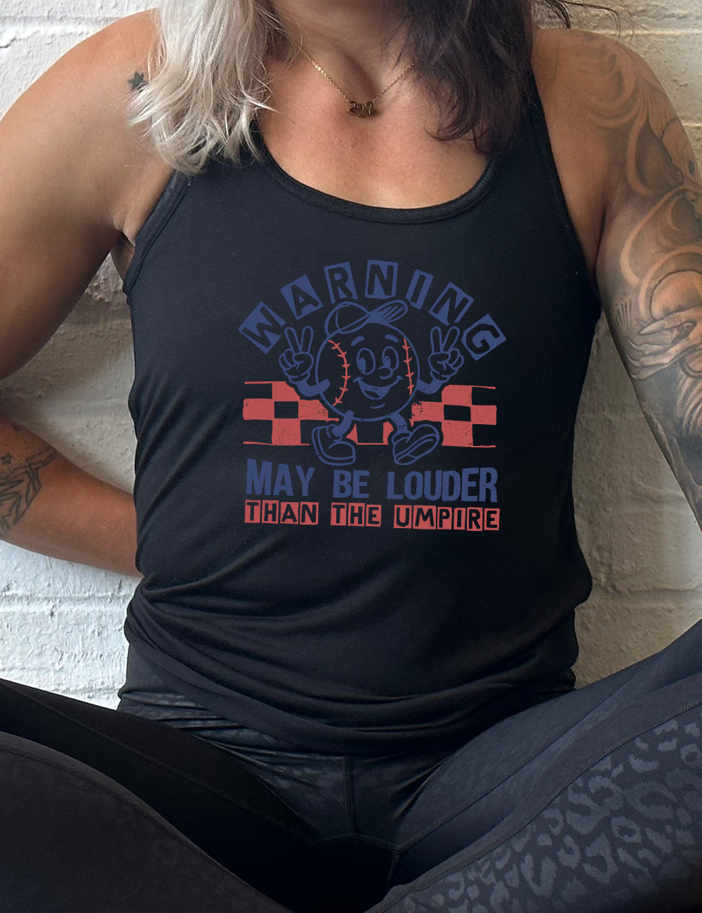 black flowy racerback tank with the words "warning may be louder than the umpire" on it, with the graphic of baseball with a face, wearing a hat, holding up two peace signs, and walking along, with a checkered border behind it