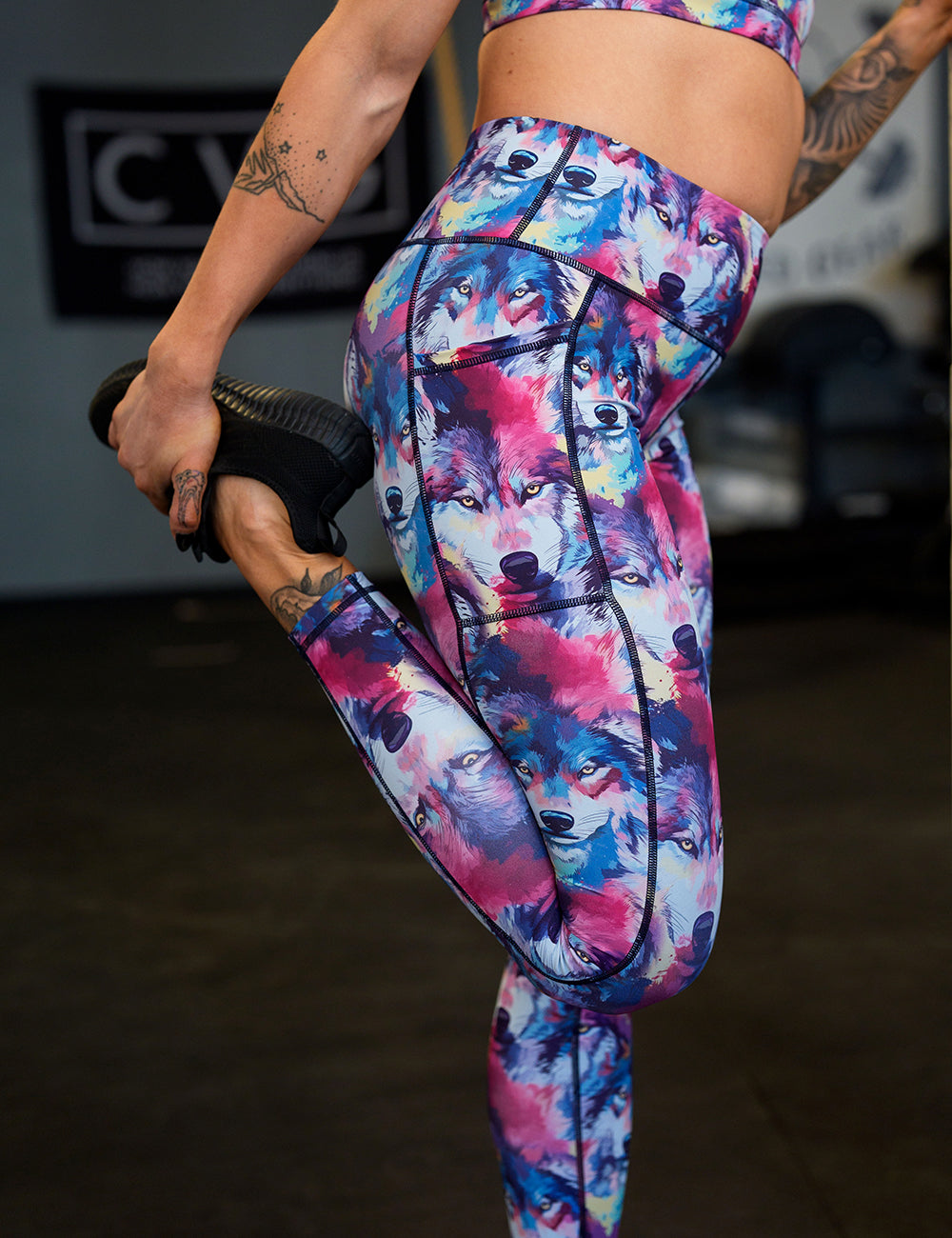 model wearing the red, blue, white, and yellow watercolor style wolves full length leggings stretching in the gym