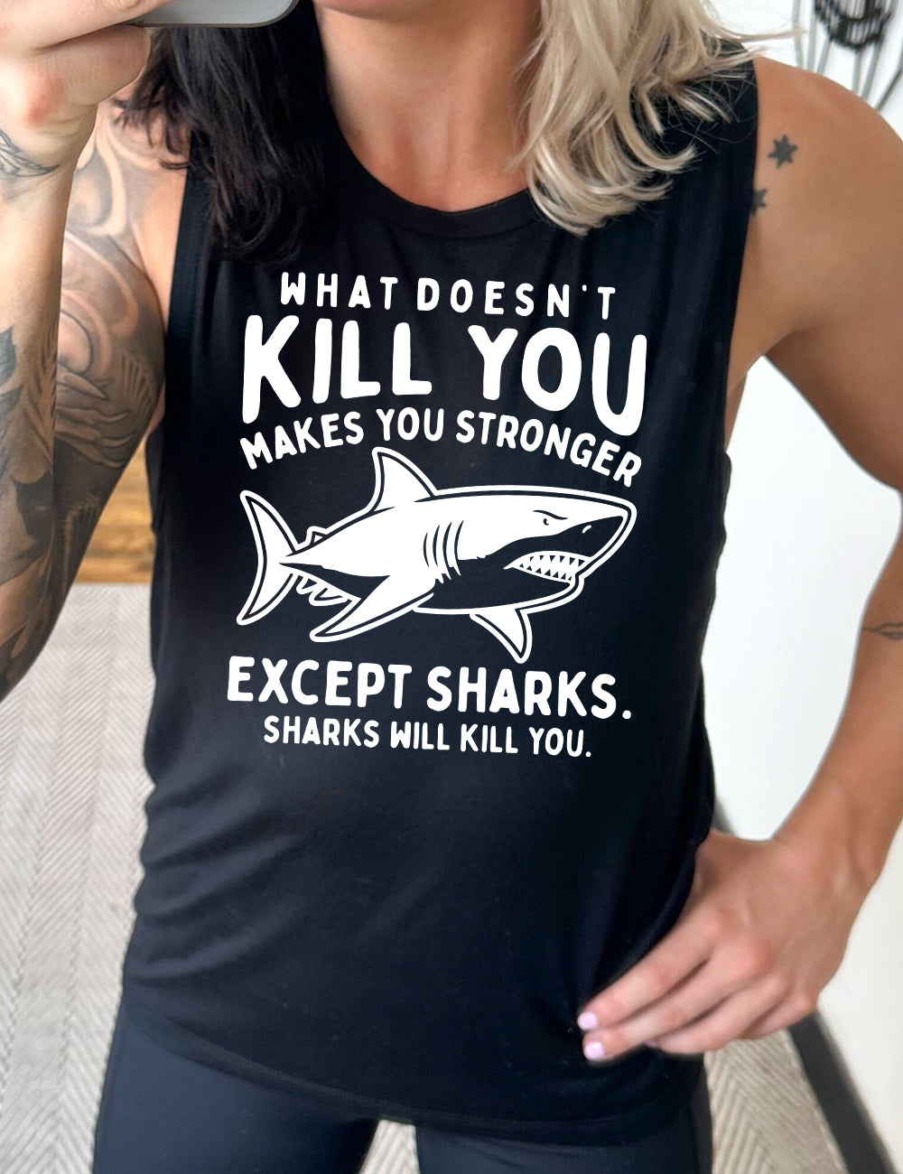 black muscle tank with the words "what doesn't kill you makes you stronger except sharks. sharks will kill you." and the graphic of a fierce shark in the middle