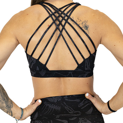 back view of butterfly back strap design on black sports bra with grey dinosaur skull and bones