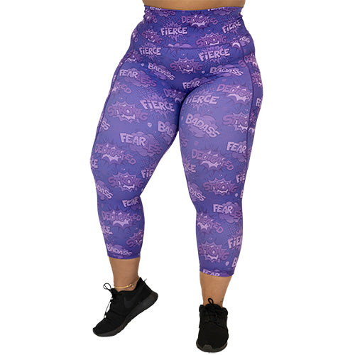 front view of capri length purple leggings with comic book style action bubbles that say "badass", "fierce" and "dedication"