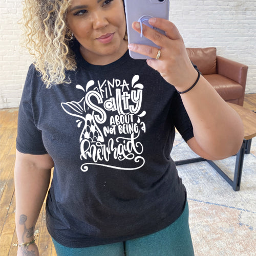 Model wearing a black unisex tee with the saying "kinda salty about not being a mermaid" in the center