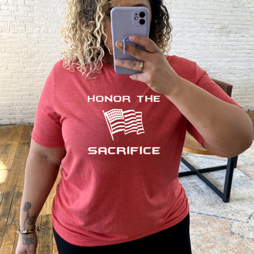 model wearing a red unisex shirt with the saying "honor the sacrifice" and an American flag in white