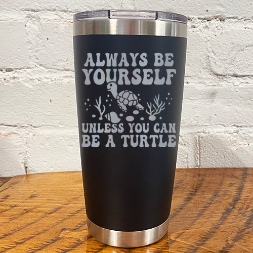 20oz black tumbler with silver saying "always be yourself unless you can be a turtle" with turtle cartoon, seaweed, shells and bubbles