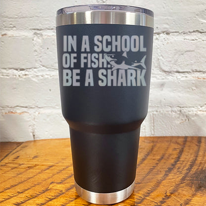 30oz black tumbler with silver saying "in a school of fish be a shark" with a shark cartoon over the word "fish"