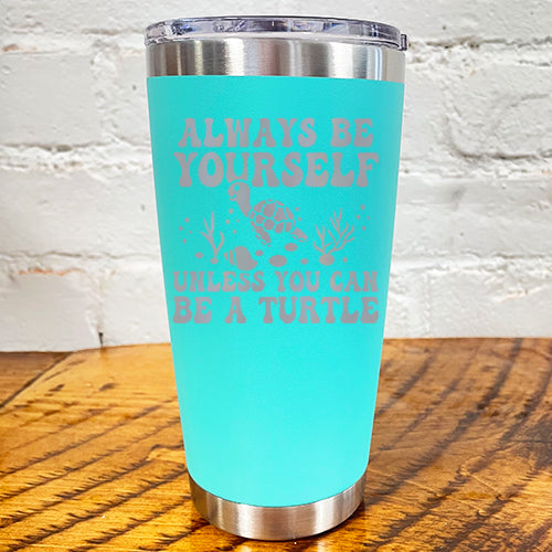 20oz teal blue tumbler with silver saying "always be yourself unless you can be a turtle" with turtle cartoon, seaweed, shells and bubbles